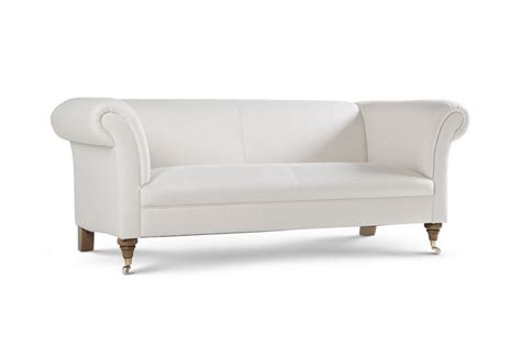 A White Couch Sitting On Top Of A White Floor Next To A Wooden Leg Chair