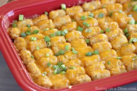 A Red Casserole Dish Filled With Tater Tots And Green Onion Garnish