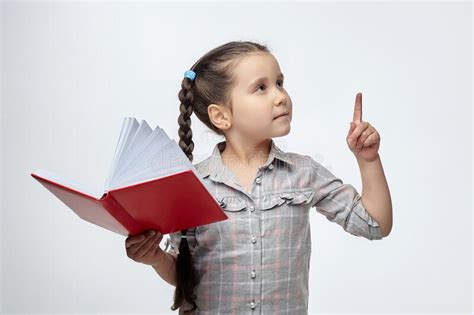 Little Black Haired Girl Holds A Red Book In Her Hands And Points To The Free Space With Her
