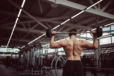 Rear View Of Young Man With Bar Flexing Muscles In Gym Stock Photo