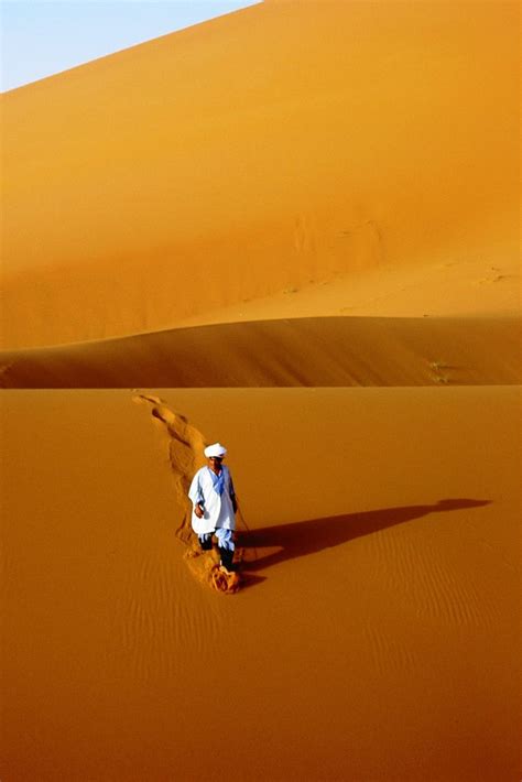 A Man Kneeling Down In The Middle Of A Desert Area With Sand Dunes