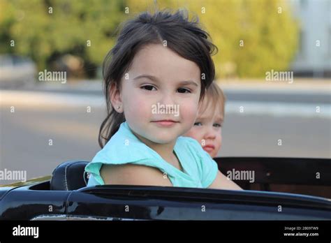 two amazing girls ride in one big toy car on city street asphalt outdoor driving in a summer