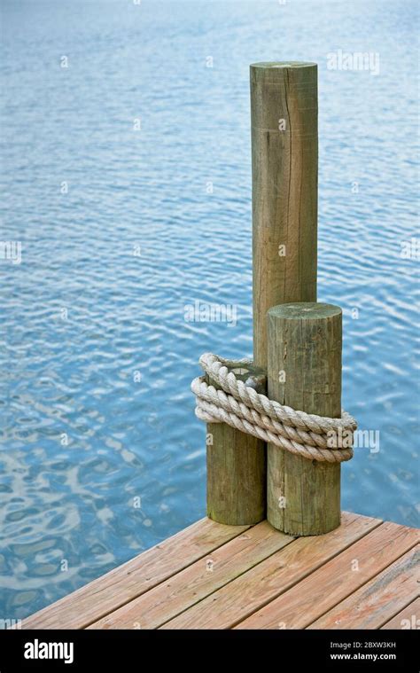 The Corner Of A Boat Dock On A Lake With Rope Wrapped Around Pilings