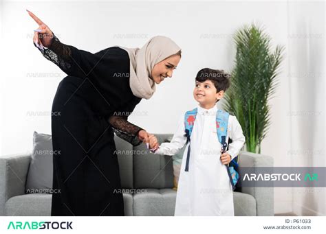 طفل عربي خليجي سعودي يرتدي حقيبة الظهر المدرسية، ارتداء الزي المدرسي، أم تمسك بيد طفلها وتشير
