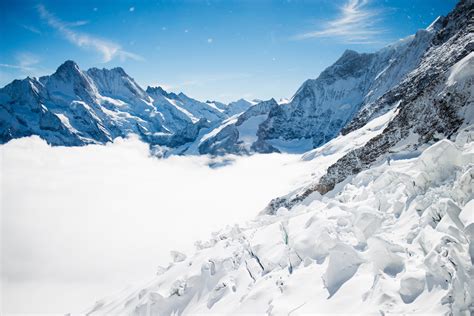 Snowy Plain Surrounded By Snow Covered Mountains With A Bright Blue Sky