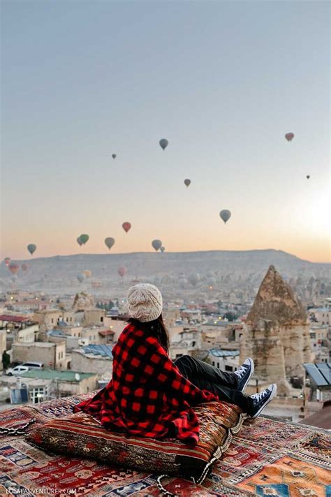 A Person Sitting On Top Of A Rug Looking At Hot Air Balloons In The Sky