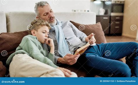Doing Homework Together Grandad And Grandson Sitting On Sofa In The