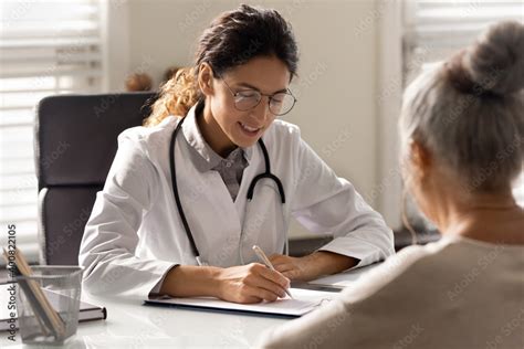 Smiling Young Woman Gp Write Prescription To Mature Patient At