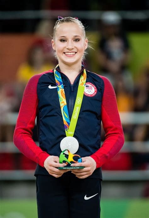 A Woman Holding A Medal And Smiling At The Camera With Her Hands On Her