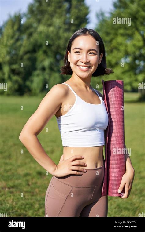 smiling fitness girl with rubber mat stands in park wearing uniform for workout and sport