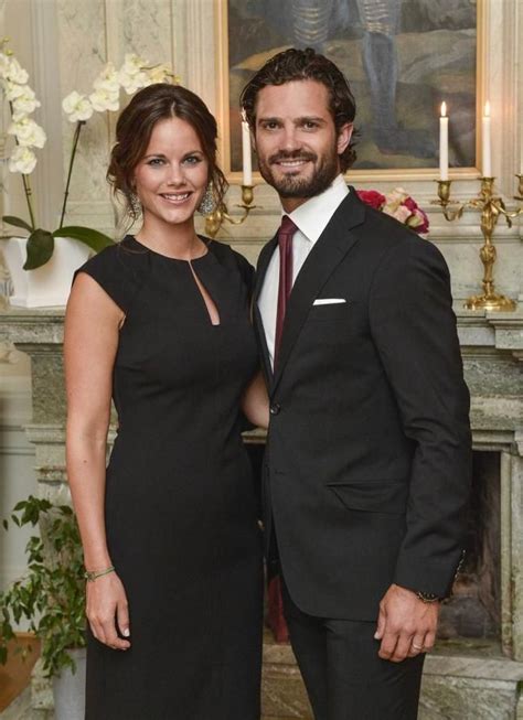 A Man And Woman Standing Next To Each Other In Front Of A Fireplace