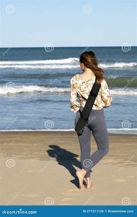 Young Woman Seen From Behind Standing On The Beach Looking Out To Sea