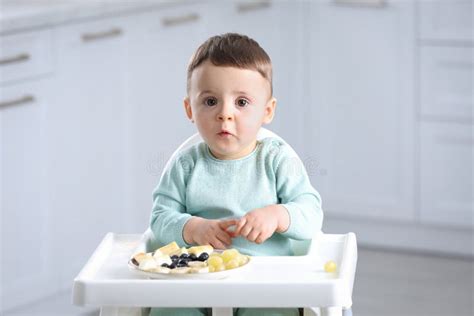 Cute Little Baby Eating Healthy Food In High Chair At Home Stock Image