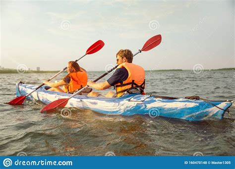 Happy Couple Kayaking On River With Sunset On The Background Stock