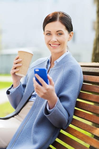 Koncepcja Biznesu I Ludzi Młoda Uśmiechnięta Kobieta Ze Smartfonem Siedząca Na ławce I Pijąca