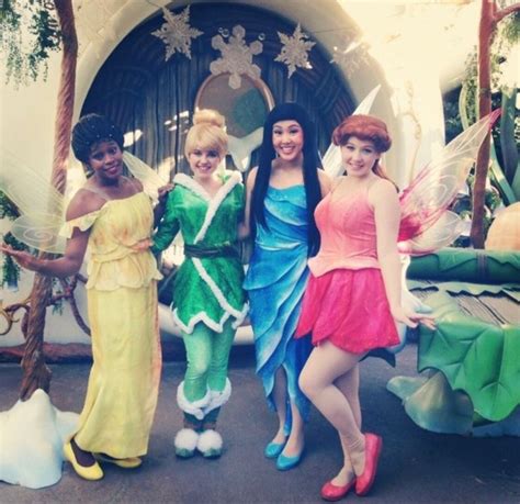 three women dressed as tinkerbells pose in front of a fairy land entrance