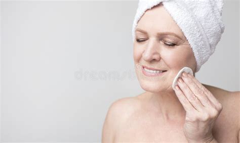 Mature Woman With Towel On Head Cleaning Her Face With Lotion Stock