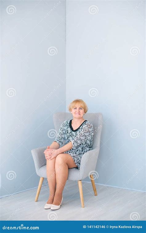 Beautiful Senior Woman Sitting On Armchair In Light Blue Studio Stock