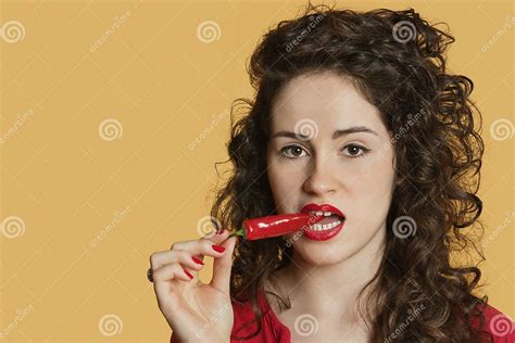 Portrait Of A Young Woman Biting Red Chili Pepper Over Colored