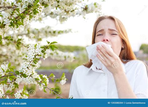 Outdoor Shot Of Displeased Caucasian Woman Feels Allergy Holds White Tissuue Stands Near Tree
