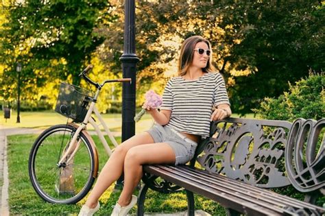 黑发女性坐在长凳上，在背景公园里拿着自行车拿着花束。动物植物免费下载格式626像素编号53998872 千图网