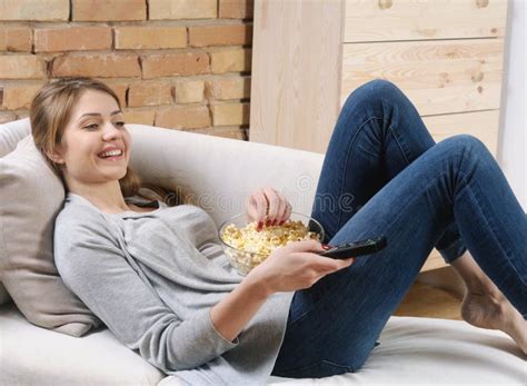 Young Woman Relaxing And Watching Tv With Popcorn On The Sofa At Stock