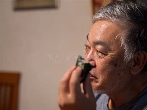 An Older Man Enjoying An `onigiri` Rice Ball In His Home Stock Image