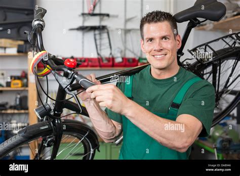Bicycle Mechanic Carrying A Bike In Workshop Smiling Into The Camera
