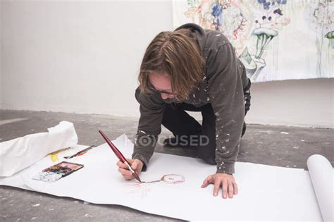 Front View Of Kneeling Creative Male Artist Working In His Workshop