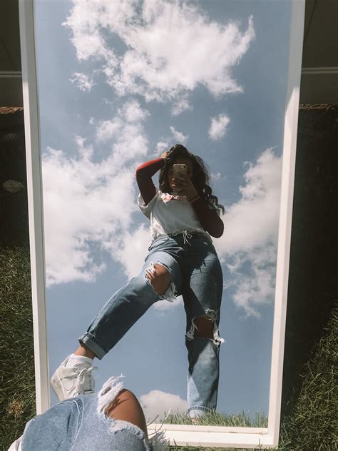 A Woman Taking A Selfie In Front Of A Mirror With Grass And Clouds