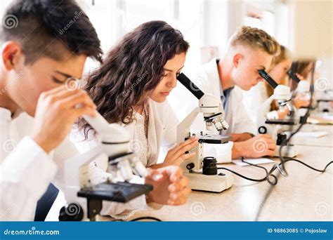 Beautiful High School Students With Microscopes In Laboratory Stock