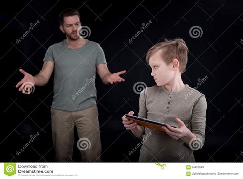 Father Gesturing And Looking At Son Using Digital Tablet Stock Image