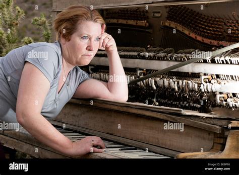 Mature Woman In Desert Setting Playing A Wooden Antique Piano With A Sad Contemplative