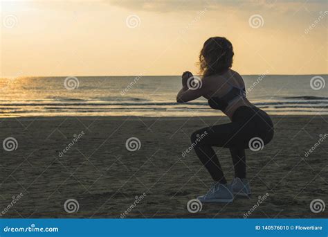sporty athletic woman in sneakers and tracksuit squatting doing sit ups on the beach on the