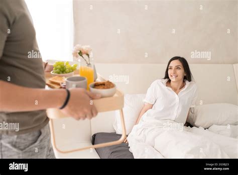 Happy Young Woman Looking At Her Husband Bringing Her Breakfast In Bed