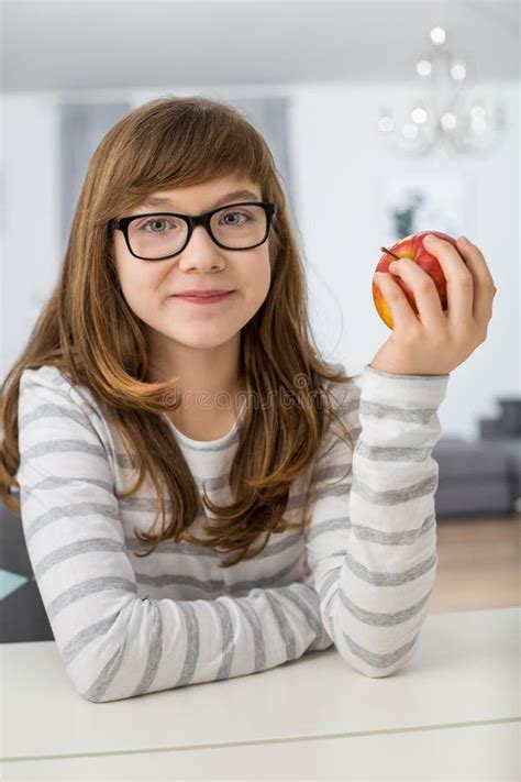 Portrait Of Teenage Girl Holding Apple While Sitting At Table In House