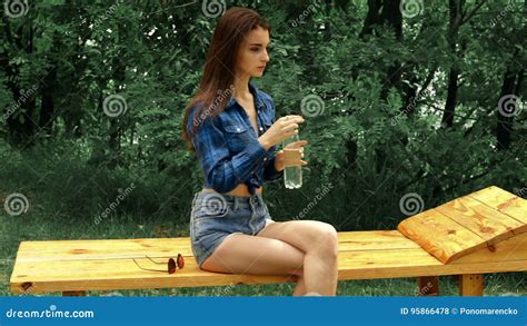 Beautiful Slim Girl Sitting On A Bench And Drink Water Stock Footage