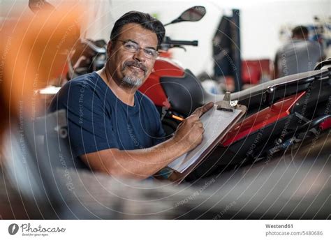 Portrait Of Smiling Mechanic With Clipboard In Motorcycle Workshop A