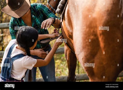 Female Rancher Helping Girl Tighten Saddle On Horse Stock Photo Alamy