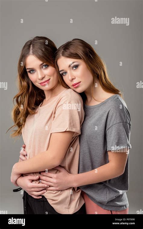 Portrait Of Beautiful Twin Sisters Hugging Each Other And Looking At Camera Isolated On Grey