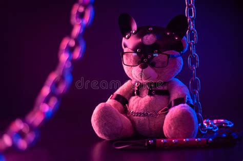 Toy Bear Dressed In Leather Belts Harness Accessory For Bdsm Games On A Dark Background In Neon