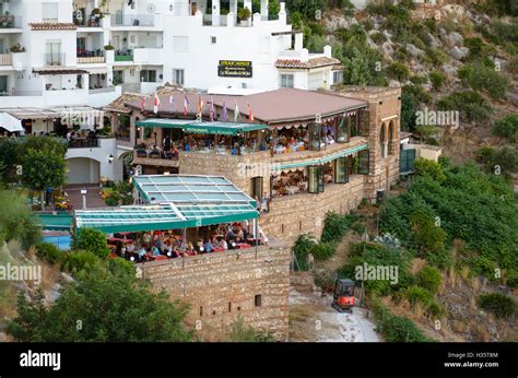 People On Terraces At Busy Restaurants Near Cliff In Spanish White