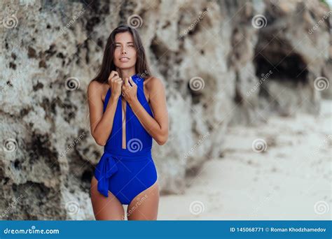 Slender Tanned Woman In Blue Swimsuit Posing On Beach With White Sand
