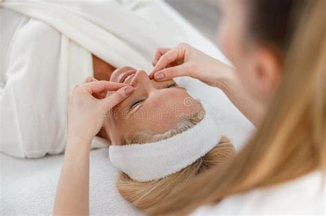 Close Up Of Female Cosmetologist Doing Facial Massage For Happy Woman Client In Spa Center Stock