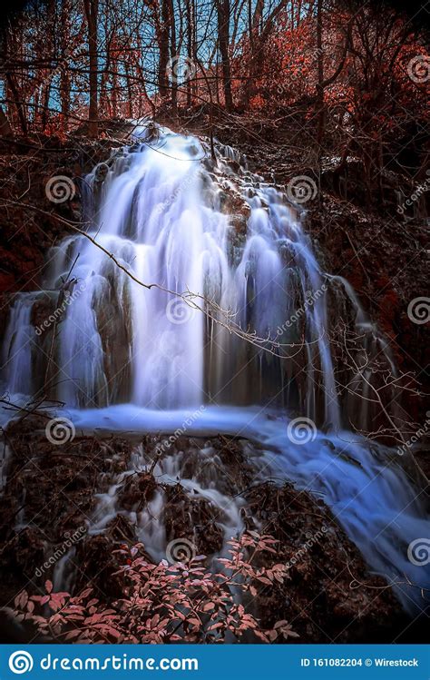 Vertical Shot Of A Magical Waterfall Flowing Through An Autumn Forest