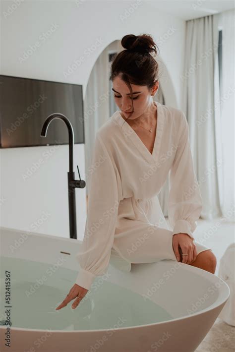 Foto De Romantic Lady Wearing Bathrobe Sitting At The Tub And Touching Water With Her Hand