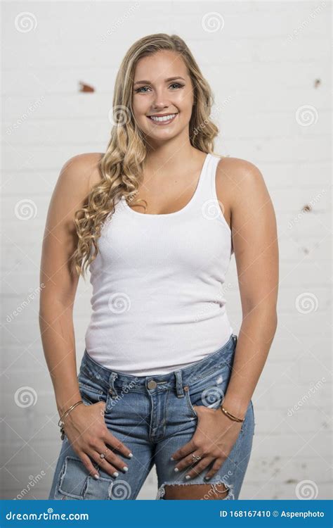 Young Blonde Woman Poses In White Tank Top And Ripped Jeans Stock Photo