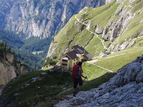 A Man Hiking Up The Side Of A Mountain With A House In The Back Ground