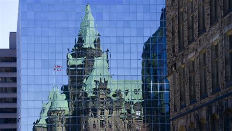 The Confederation Building reflects off the windows of a building in ...