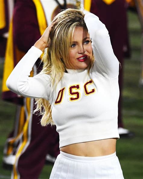 a woman in a cheerleader outfit is holding her hands up to her head while standing on the sidelines